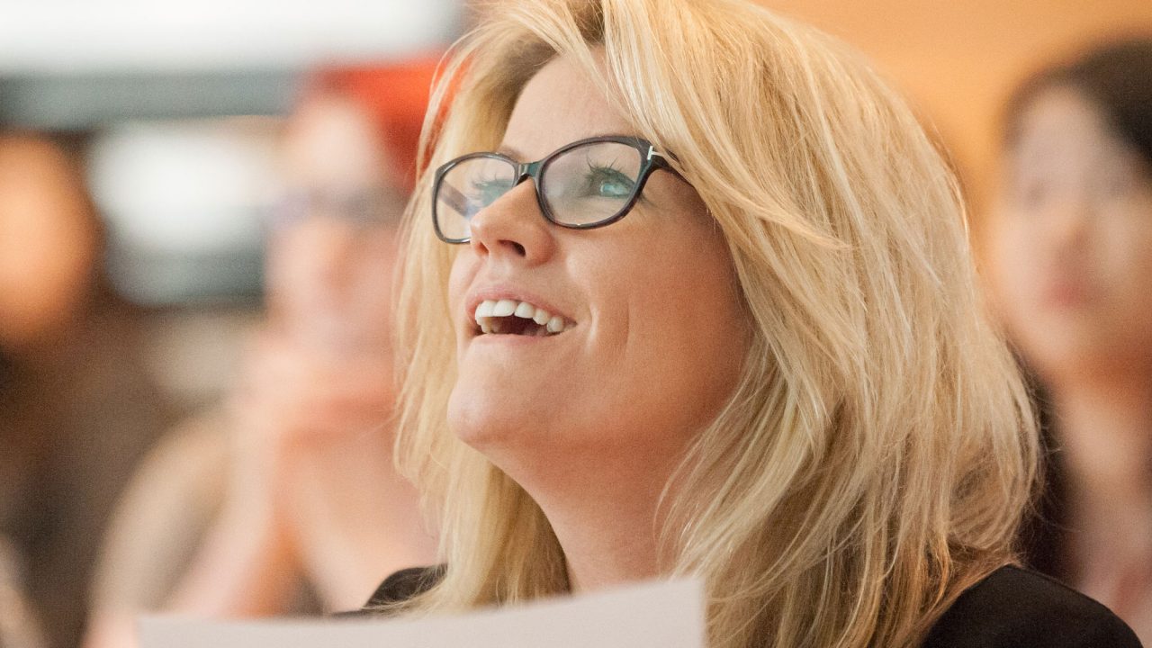 Woman with glasses holding piece of paper smiling