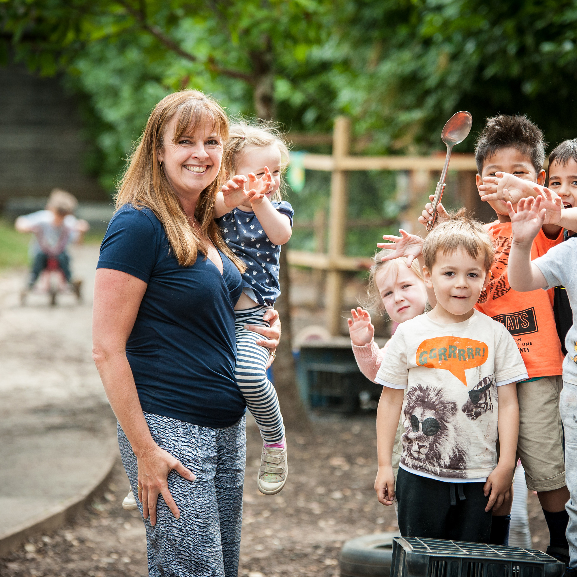 A woman holding a child and smiling into the camera whilst four other children look into the camera
