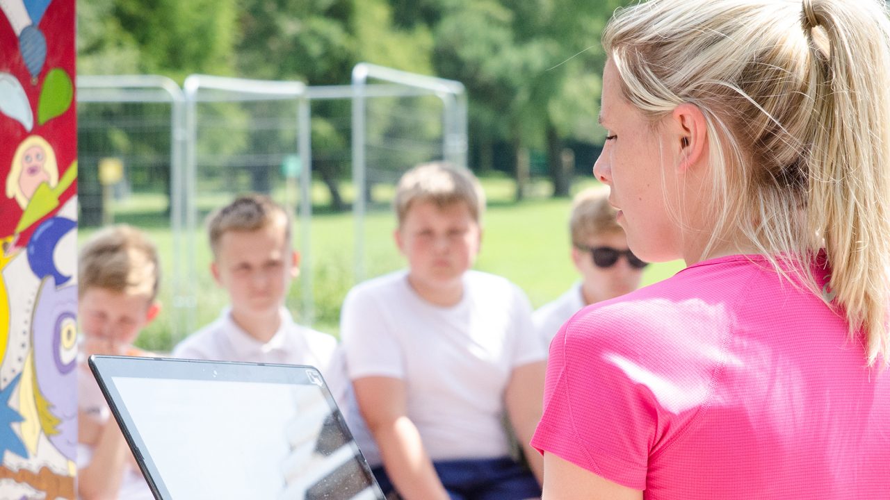 teacher holding a laptop and speaking to pupils