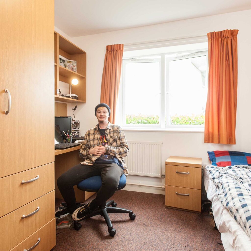 Student sat at desk smiling at camera in room at Park Challinor Halls