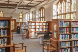 A view of the library showing rows of wooden bookshelves and Gothic style windows.