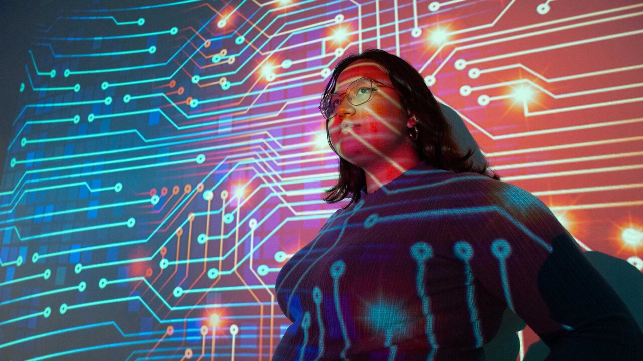 A student standing with an image of network connections projected onto her and the screen behind her.