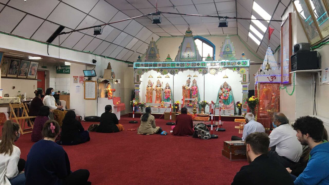 The interior of the Hindu Mandir with visitors sat on the floor.