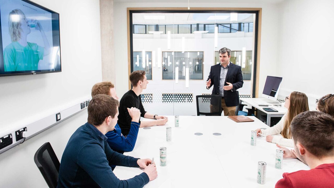 A group of student sit in a meeting room with a lecturer.