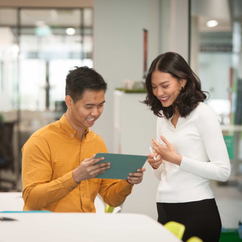 Two students look at a table together in an office environment.