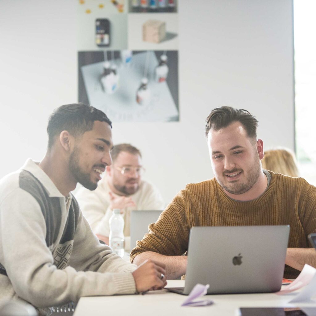 Two male students look at a laptop together.