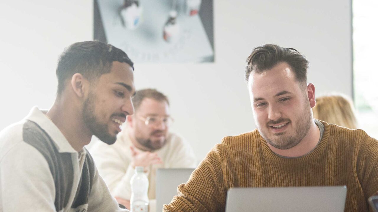 Two male students look at a laptop together.