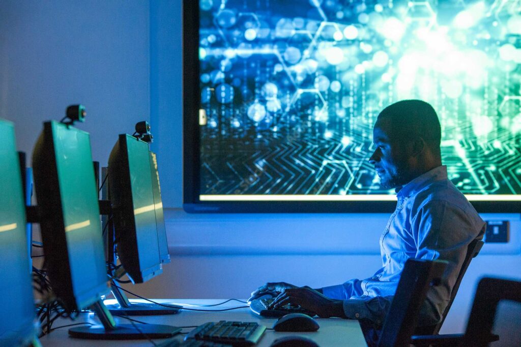 A conceptual image showing a student working at a computer with a screen showing circuitry behind him.