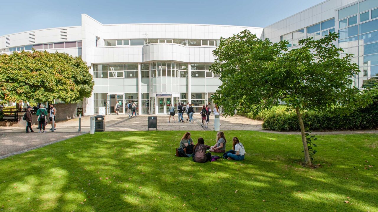 The entrance of Park Campus with students sitting on the grass outside.
