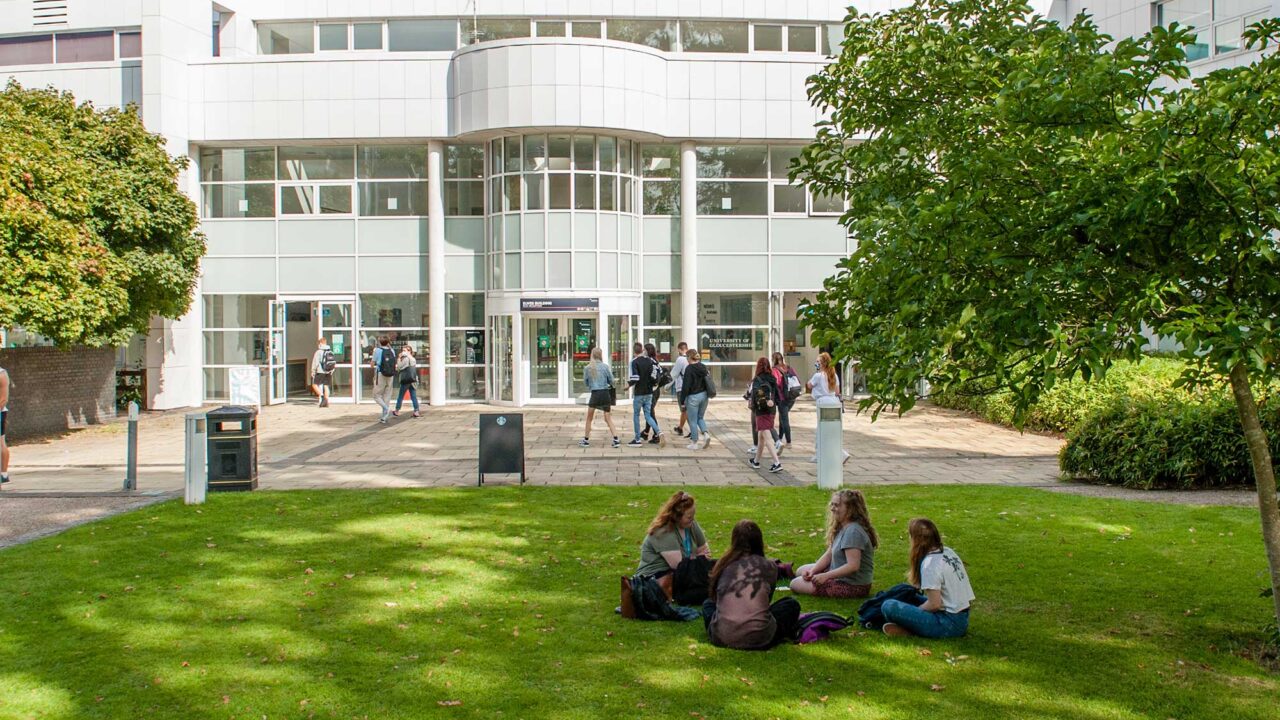 The entrance of Park Campus with students sitting on the grass outside.