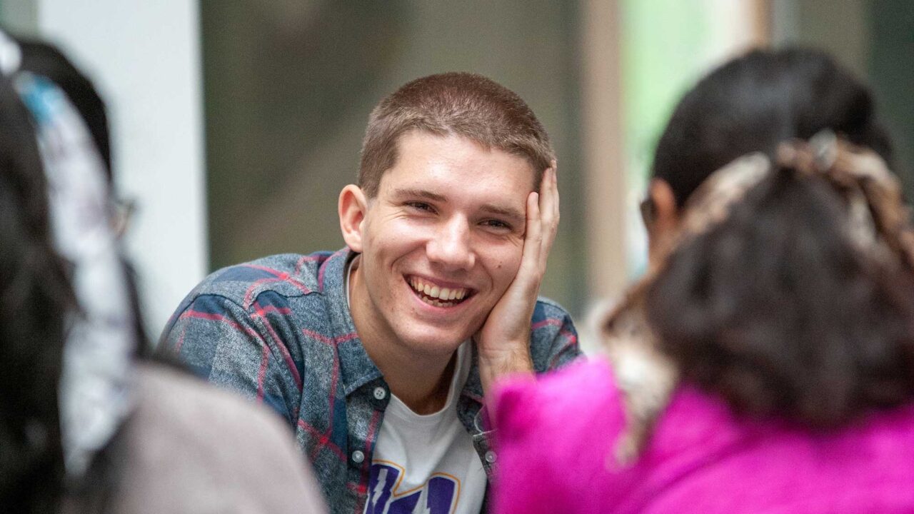 A student smiling while sat with fellow students.