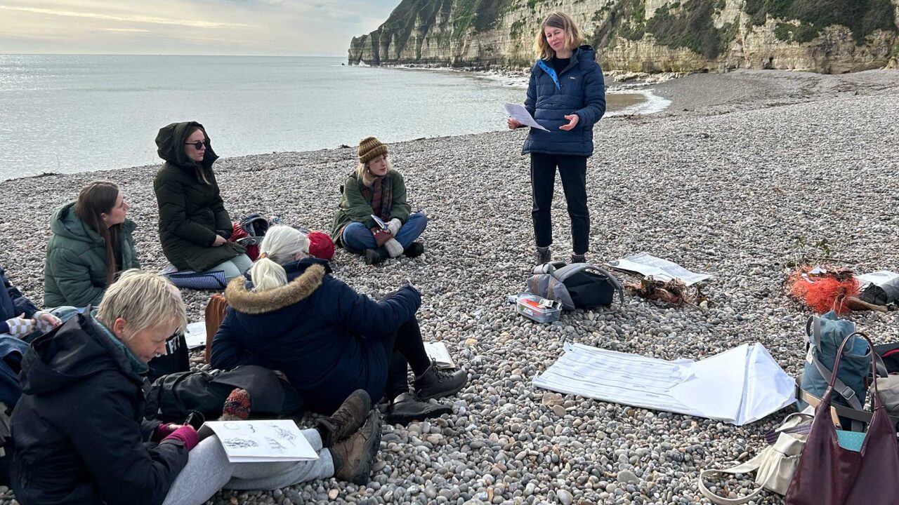 visiting-artists A group of students on a pebble beach.