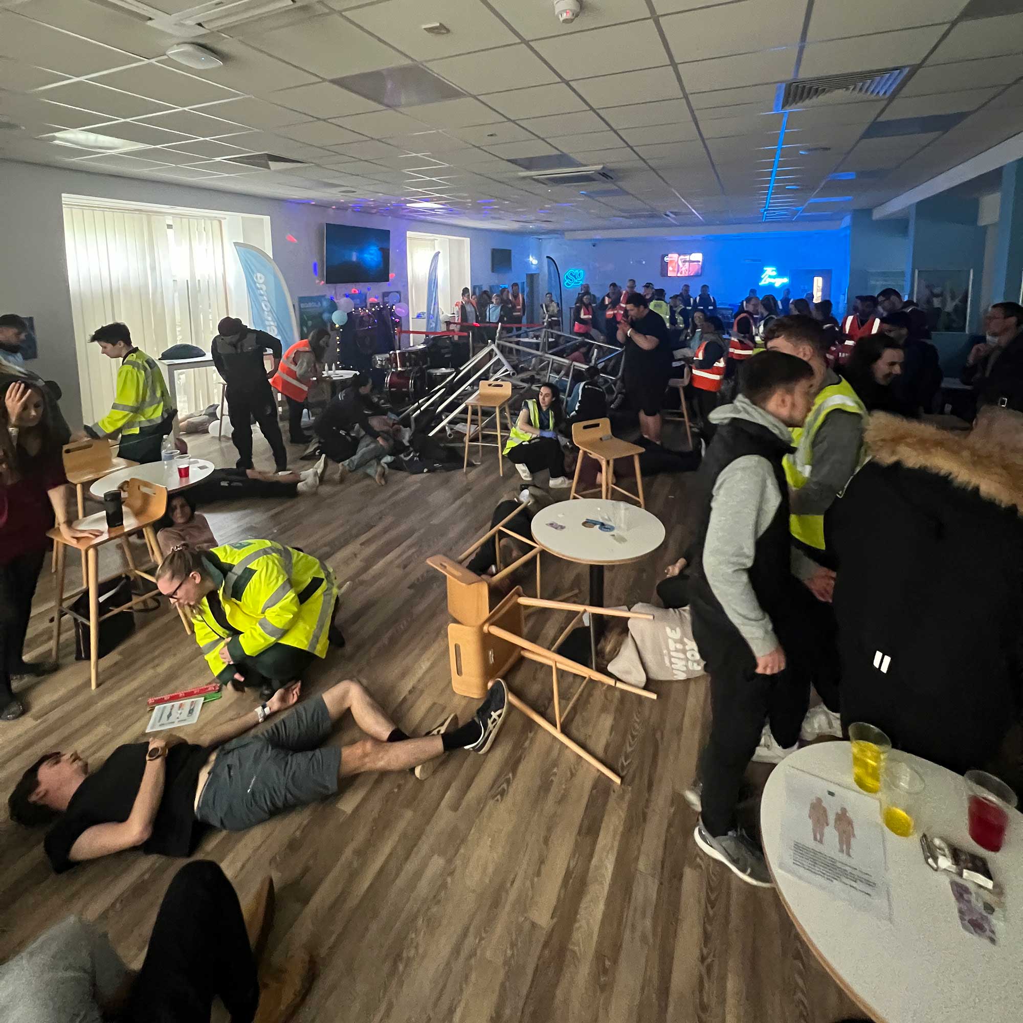 A simulated emergency showing the inside of a large room with people and chairs lying on the ground.