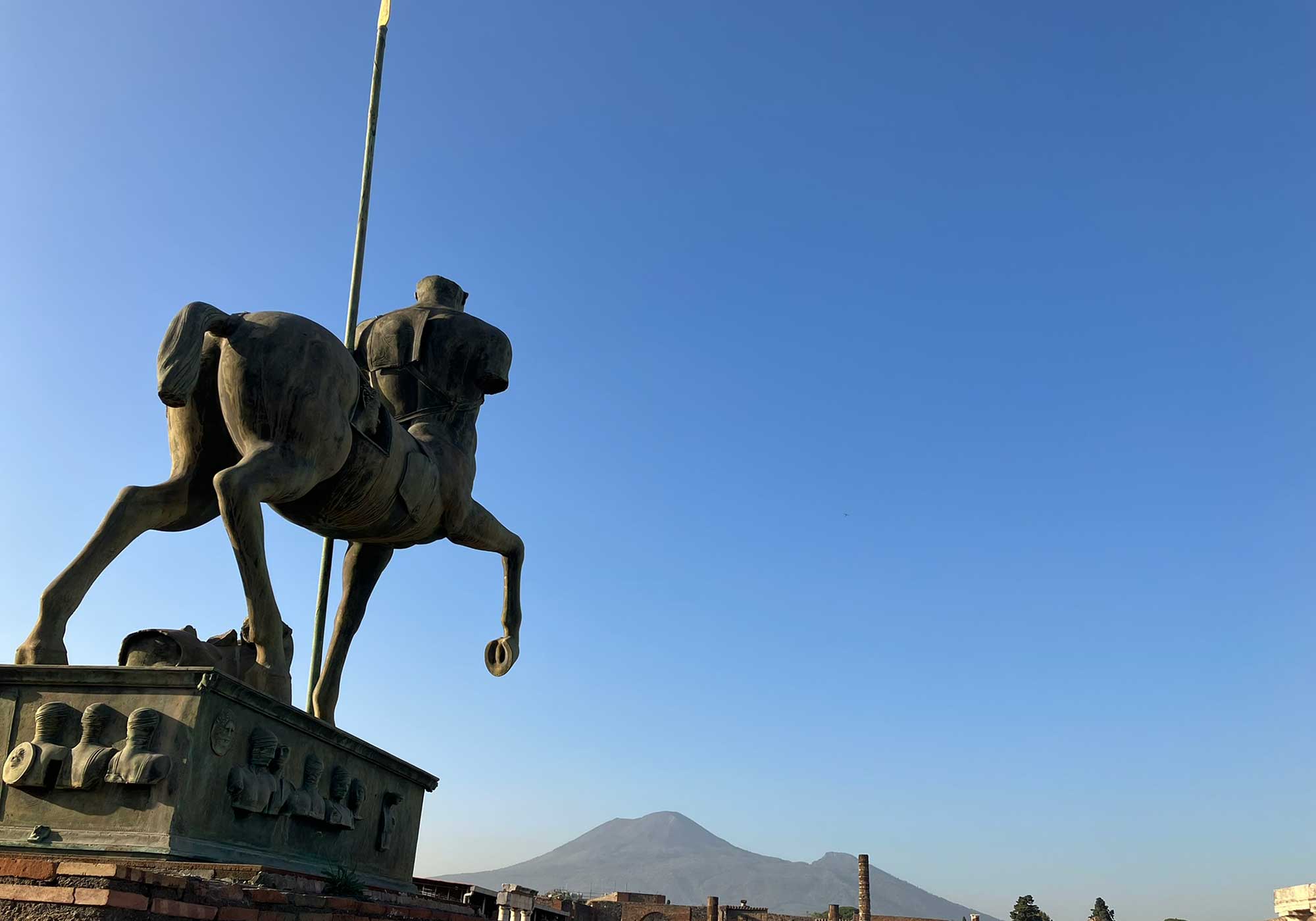 A statue in the foreground and Mount Vesuvius in the background with brilliant blue sky.