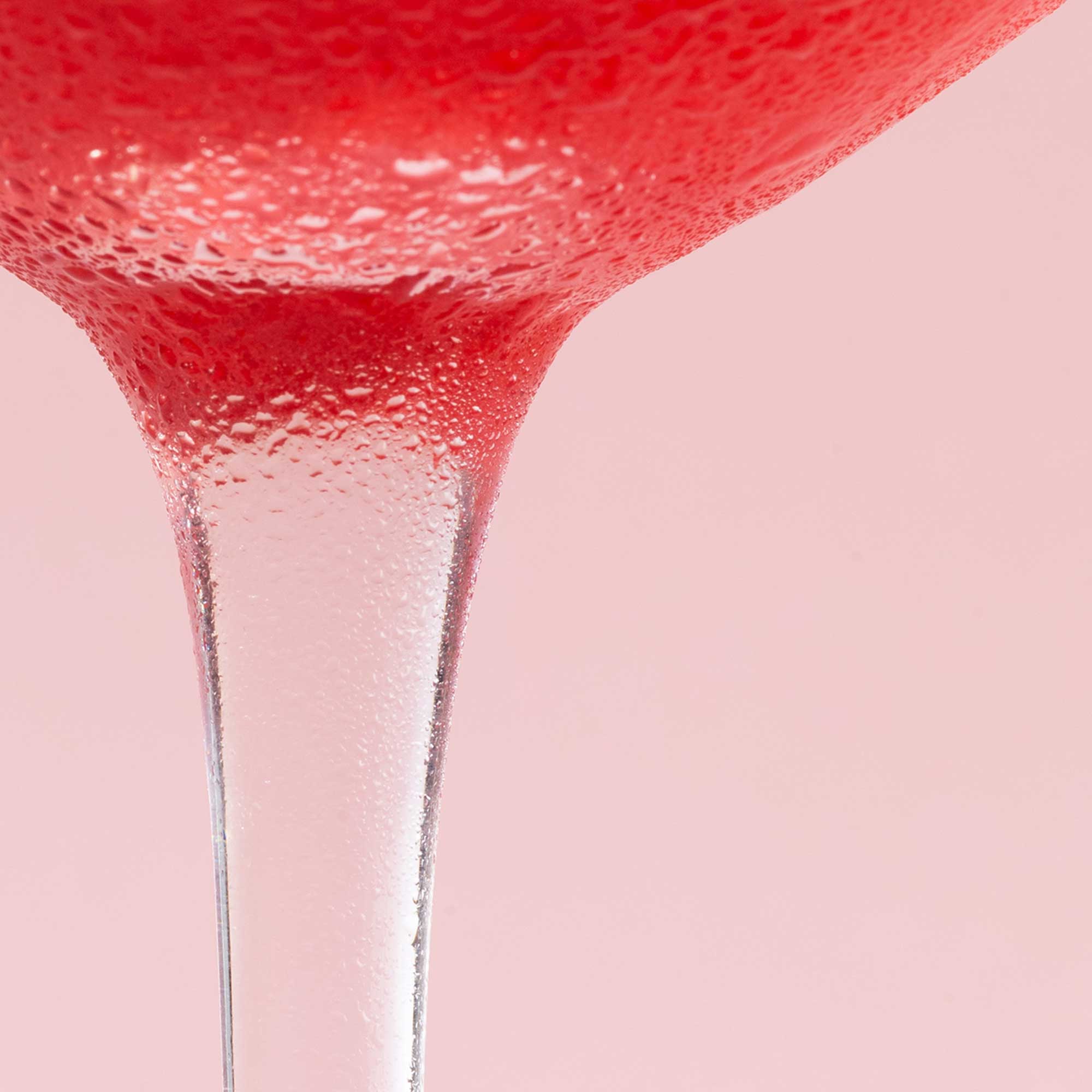 Close-up shot of a cold cocktail in a glass against a pink background.