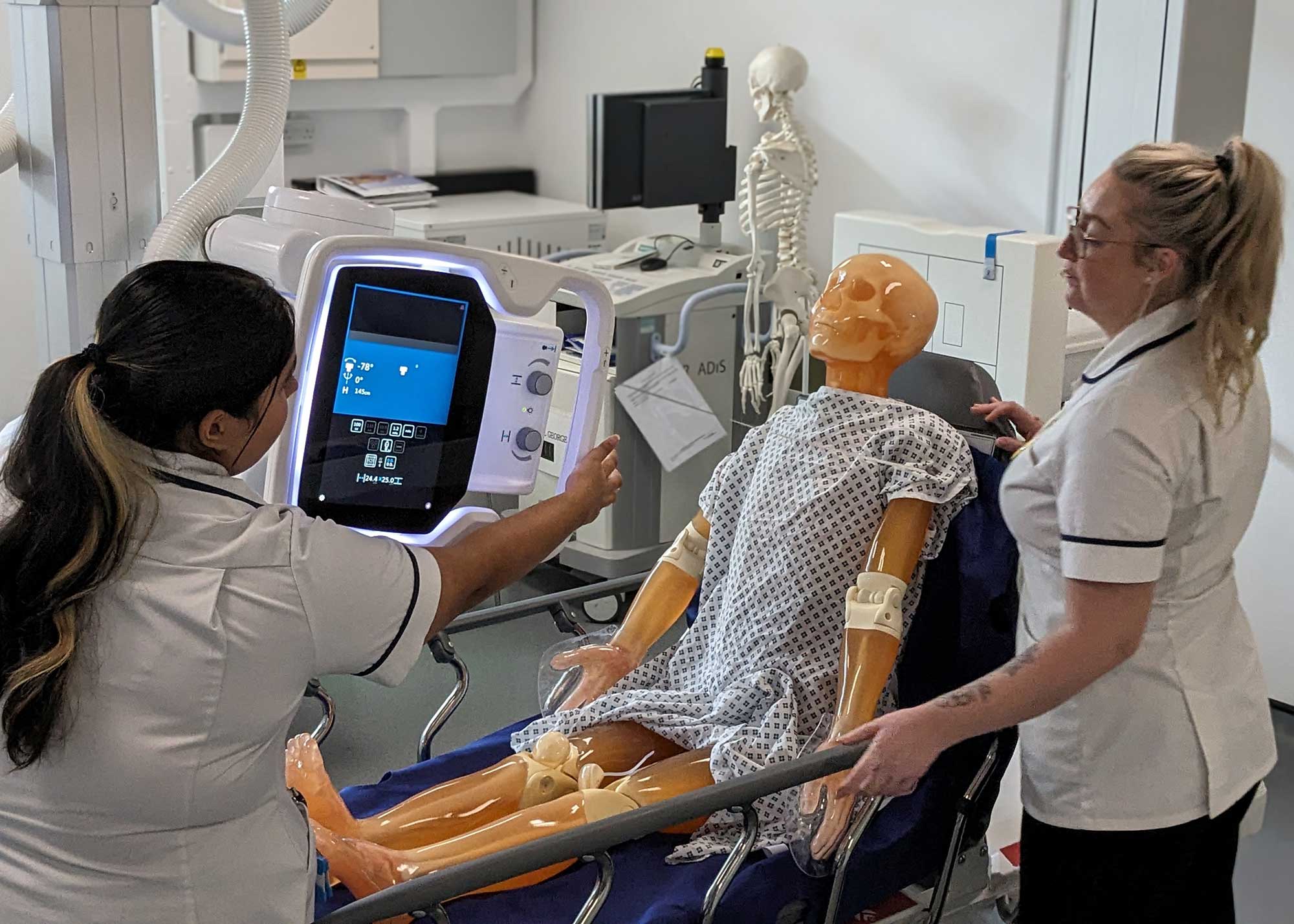 Two health and social care students use a healthcare machine in a simulation with a dummy.