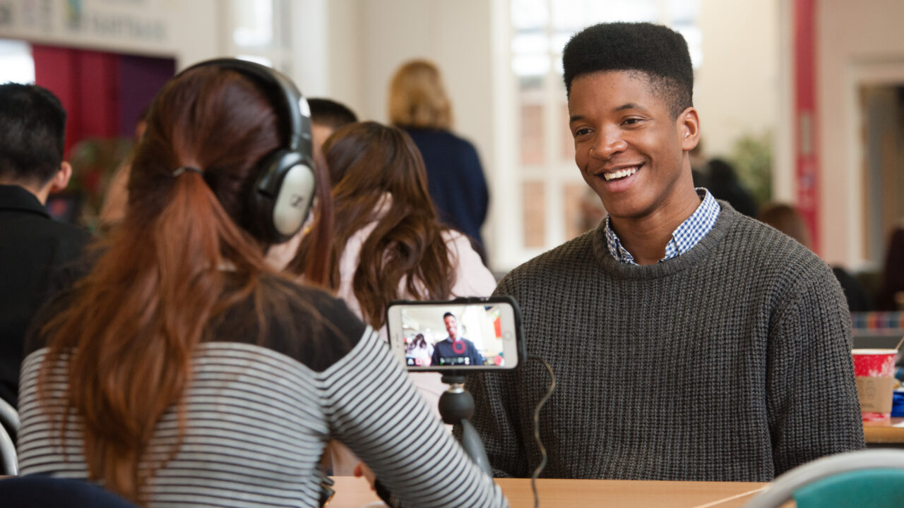 a student being filmed while being interviewed by another student - both are sat down