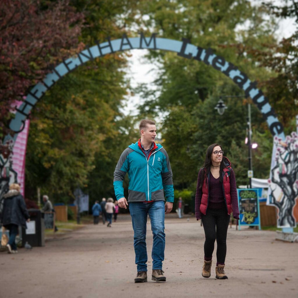 Two students walking under an arch that says 'Cheltenham Literature'.