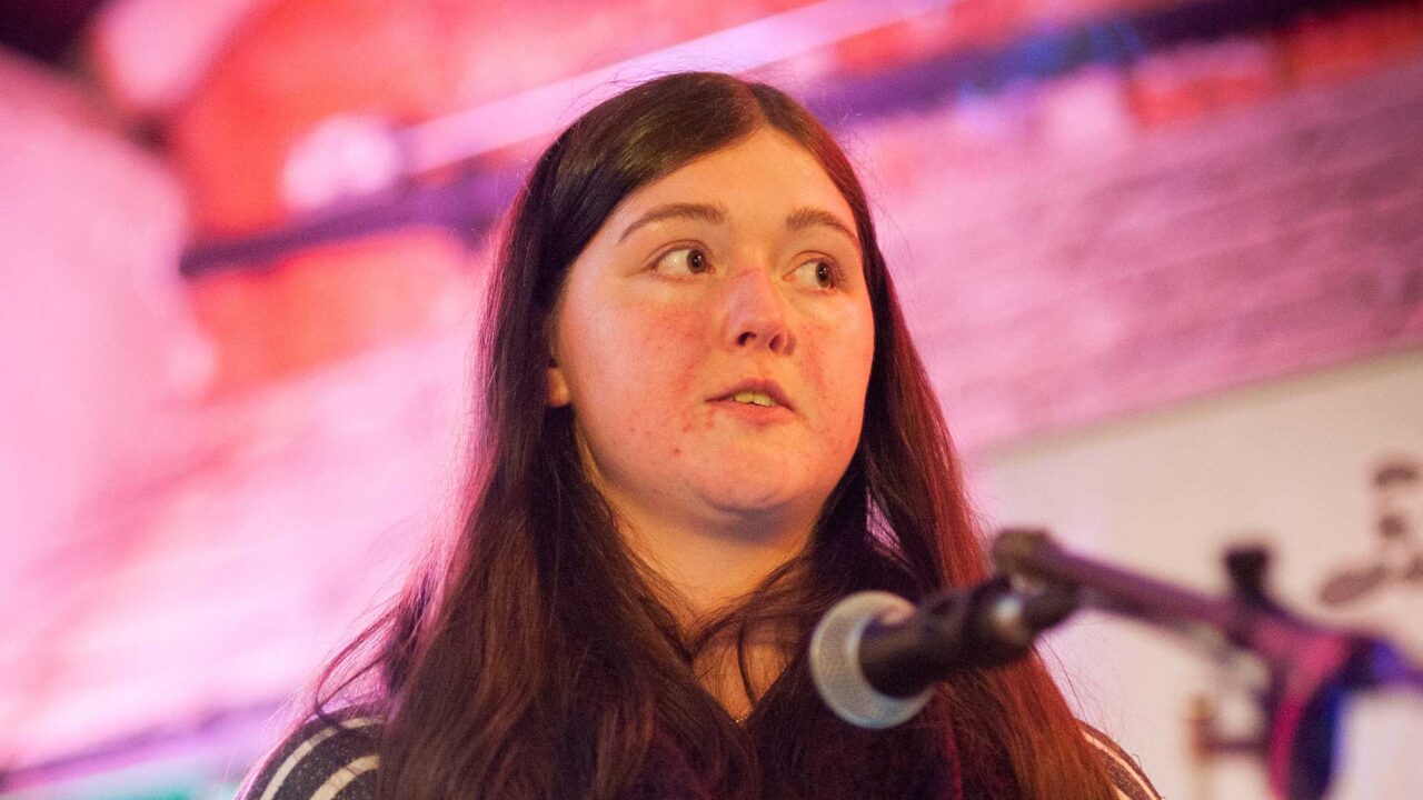 English Literature and Creative Writing student standing in front of a microphone, reading prose.