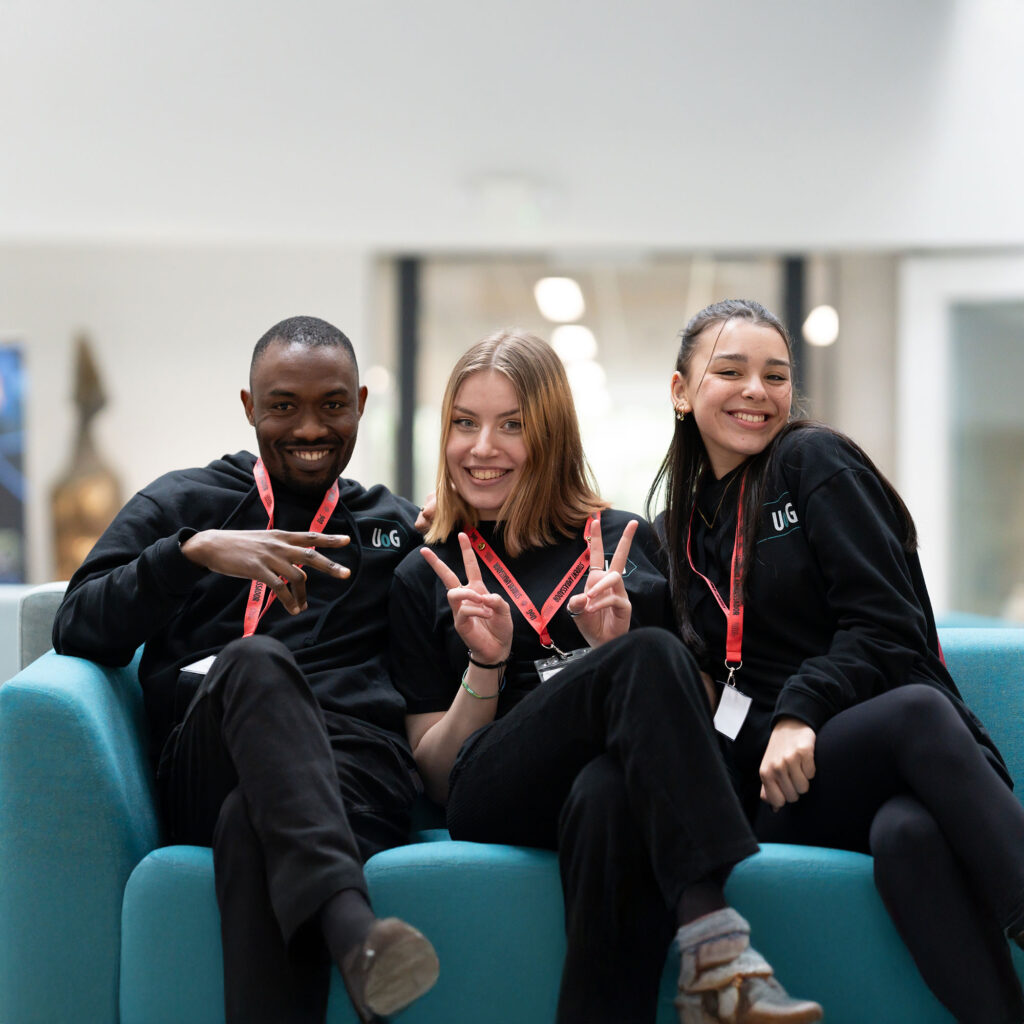 Three students sat on a sofa smiling at the camera