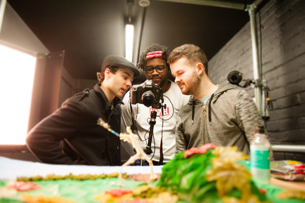 three students looking down a camera with plastic figures in the foreground