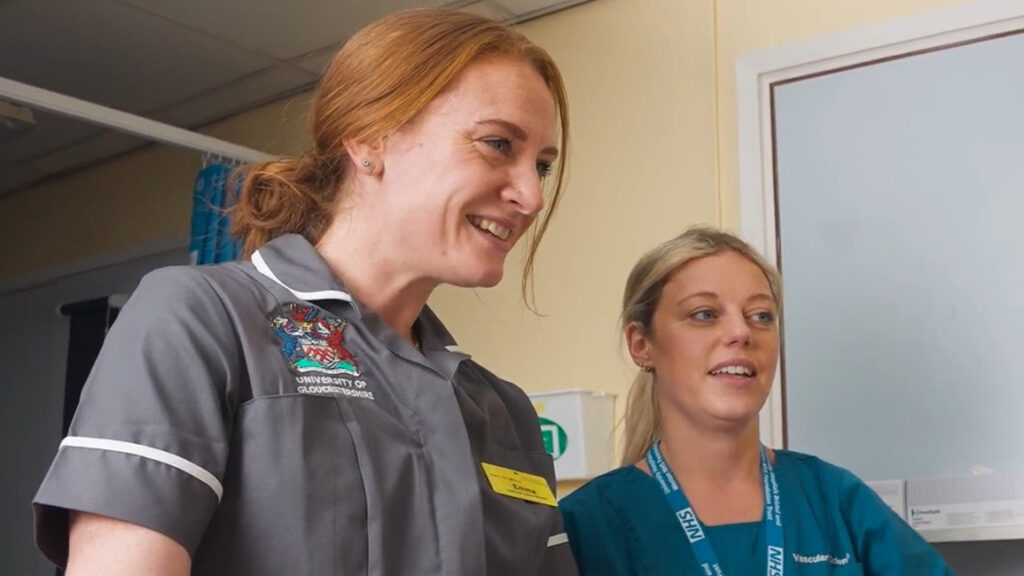 A UoG student stands alongside an NHS staff member in a clinical setting.