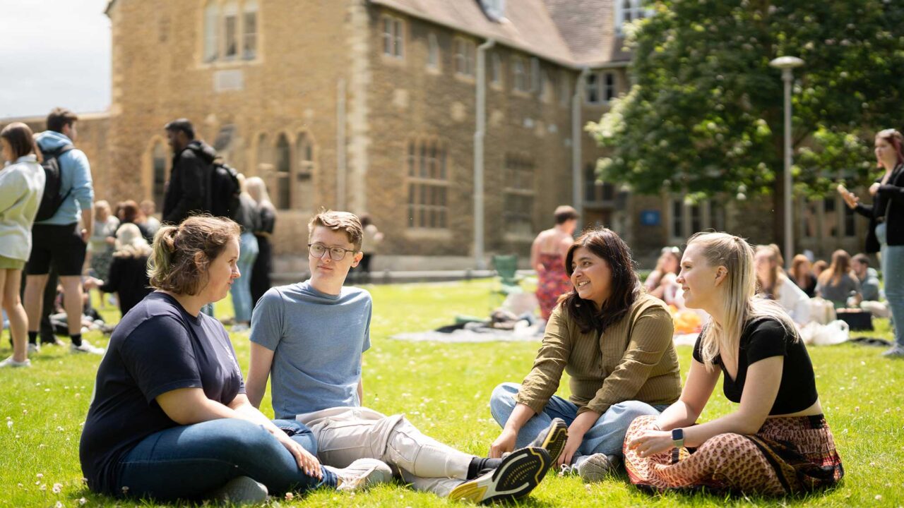 Students sitting on the grass in the sunshine at Francis Close Hall campus.