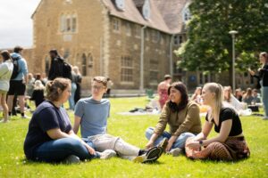 Students sitting on the grass in the sunshine at Francis Close Hall campus.