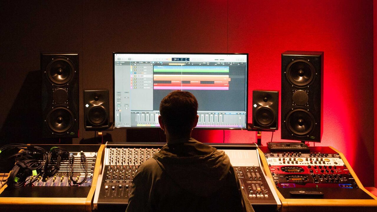 Student sitting behind an audio mixing desk.