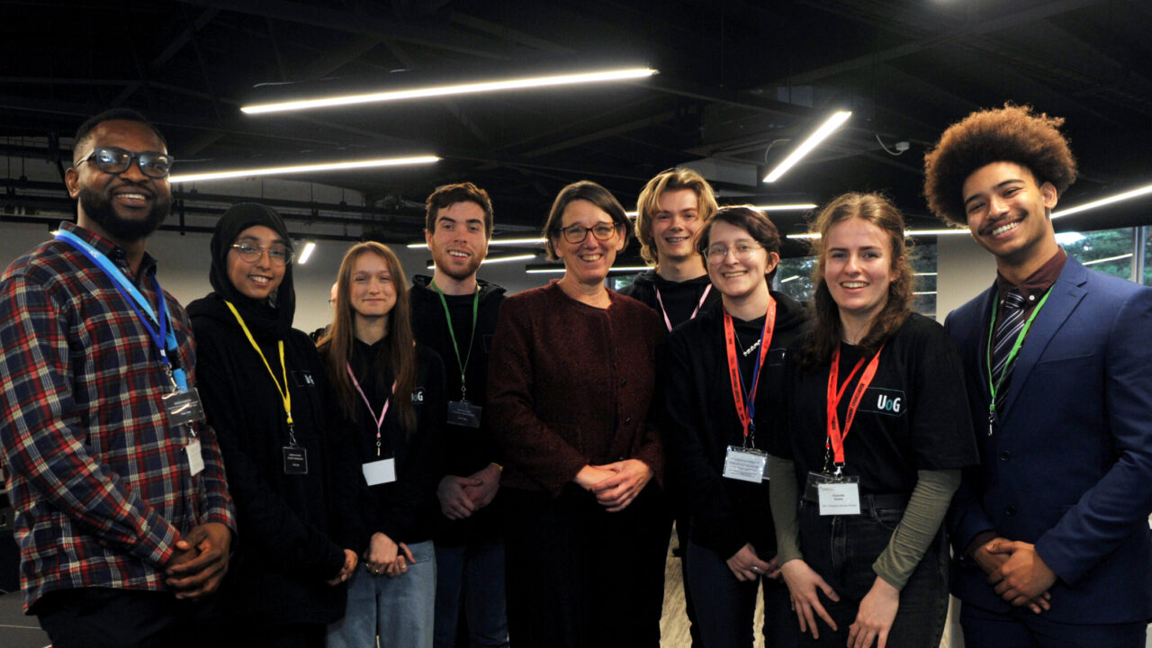 Anne Keast-Butler with eight smiling students lined up next to her looking at the camera