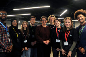 Anne Keast-Butler with eight smiling students lined up next to her looking at the camera
