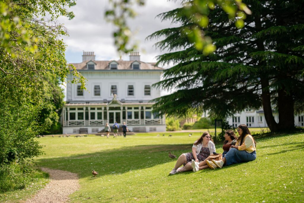 three women sat on grass with trees near them at Park Campus
