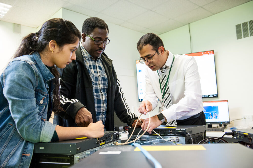 Two learners from the Cyber Security Technical Professional Apprenticeship programme examining cables with a tutor