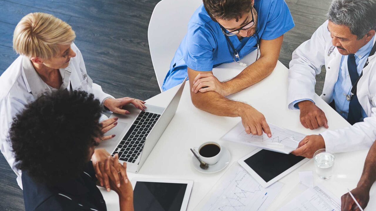 prof-doc-handsc-leadershipcarousel A group of healthcare professionals sitting around a table studying a chart.