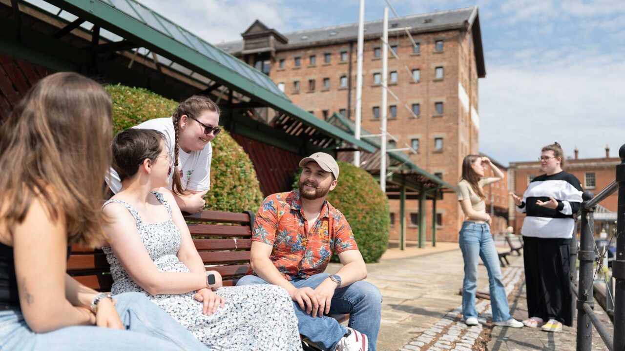 Students sitting together talking on a bench at Gloucester Docks.