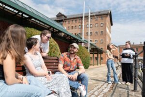 Students sitting together talking on a bench at Gloucester Docks.