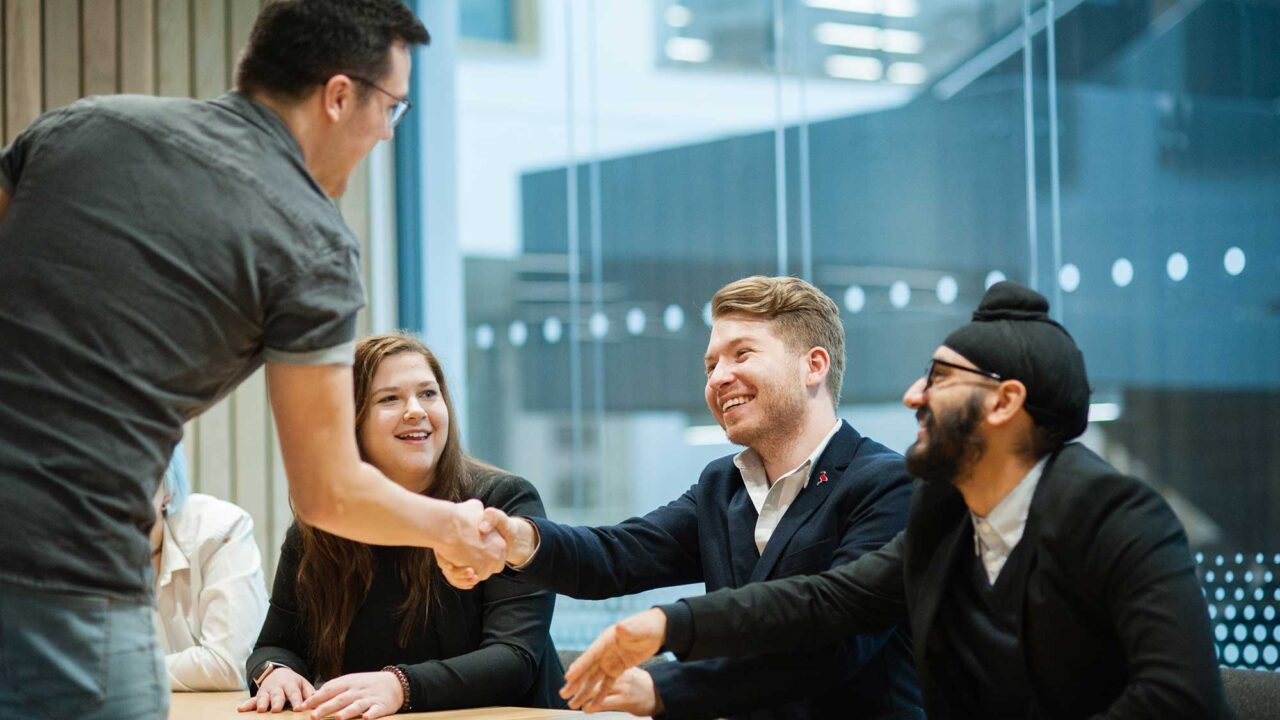 A group of young people greet a man in an office environment.