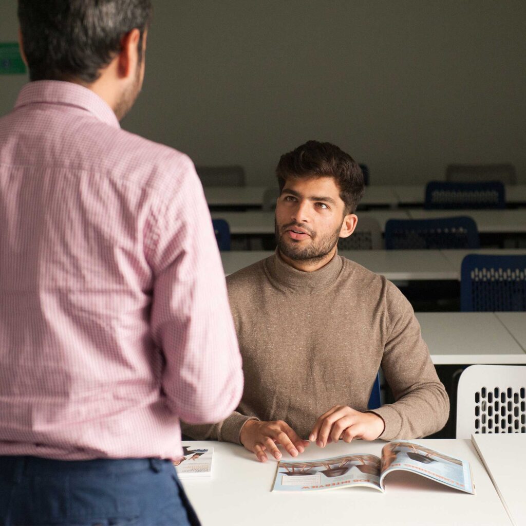 Two men chatting with magazines in front of them.