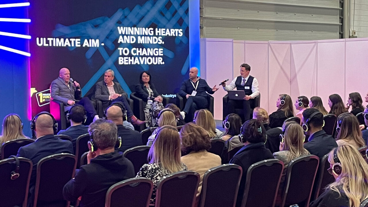 An audience listens to speakers talking on stage at an event.