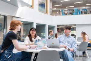 Students sit together at a table with laptops in the atrium of the Business School.