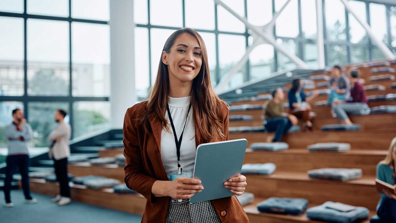 A woman stands in front of an auditorium holding a tablet pc.