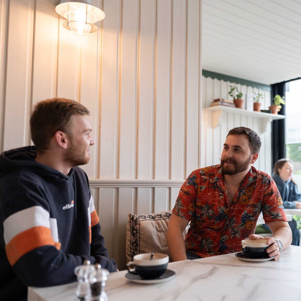 Two male students chatting over a coffee in a cafe.