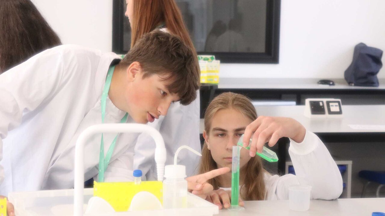 Two students wearing protective coats using lab equipment.