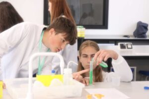 Two students wearing protective coats using lab equipment.