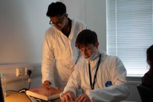 Two students wearing white overalls looking at evidence in an office.