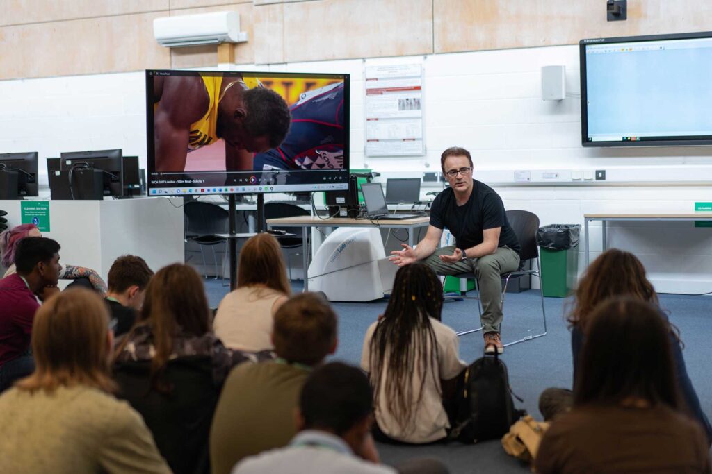 A group of students sitting on the floor listening to a teacher during a taster session.
