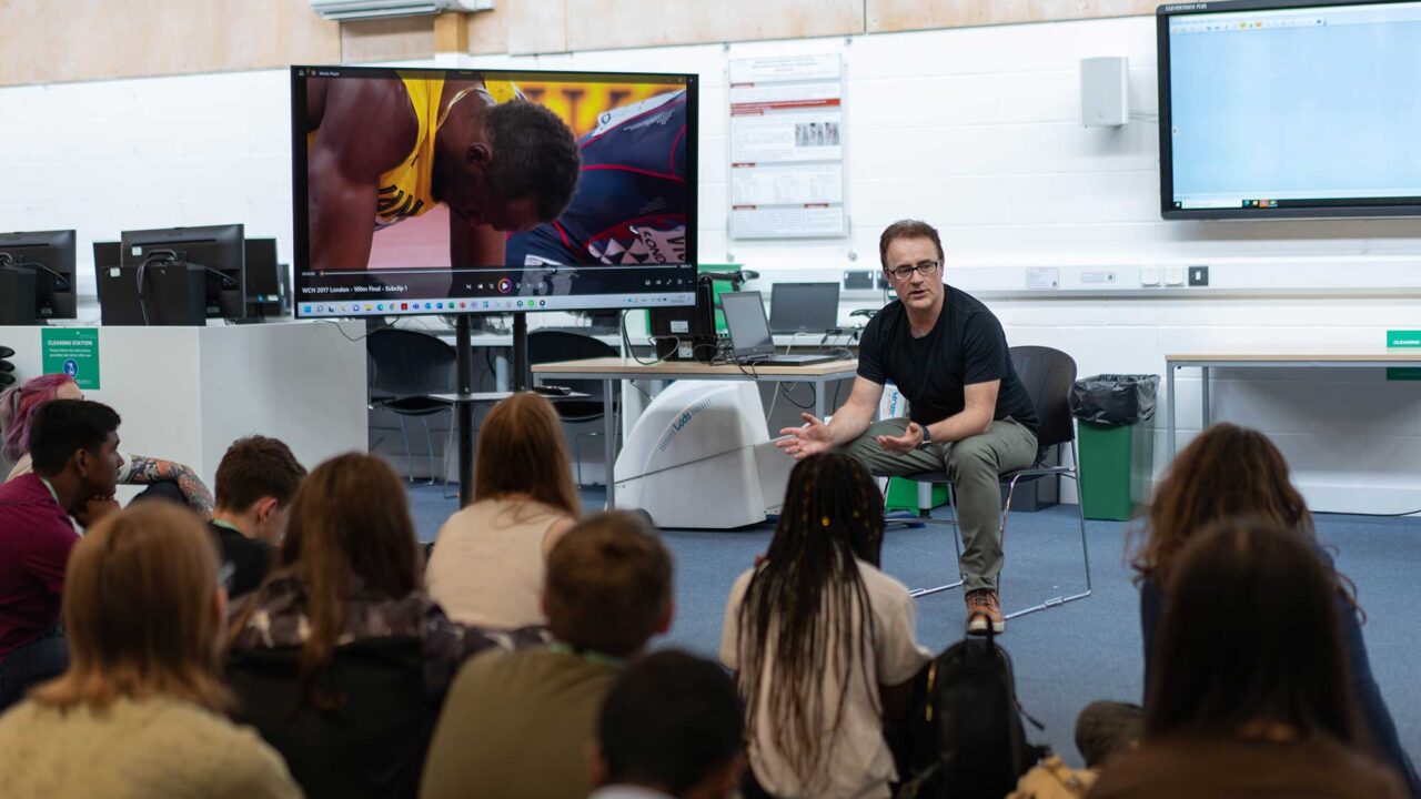 A group of students sitting on the floor listening to a teacher during a taster session.