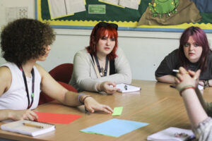 Three students sitting at desks discussing a topic together.