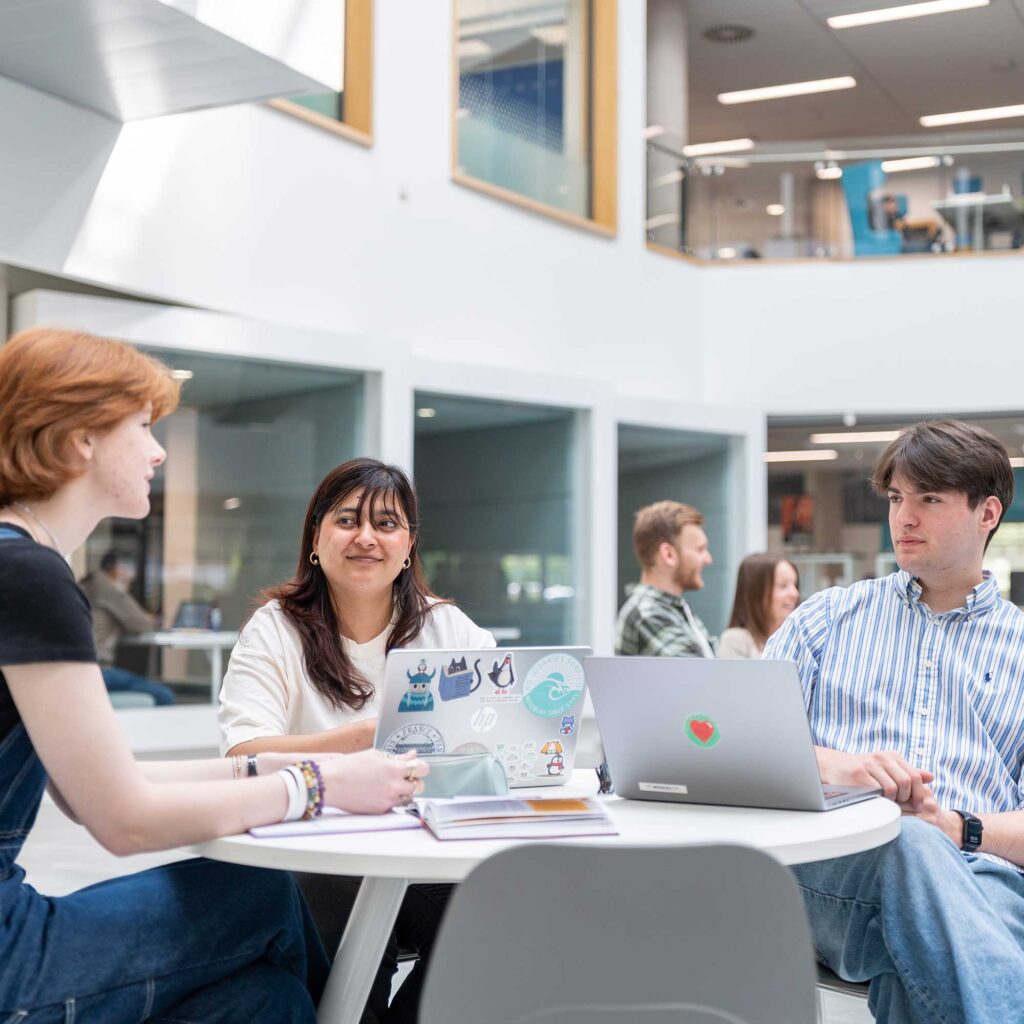 Students sit together at a table with laptops in the atrium of the Business School.