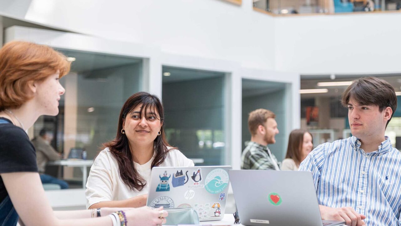 Students sit together at a table with laptops in the atrium of the Business School.